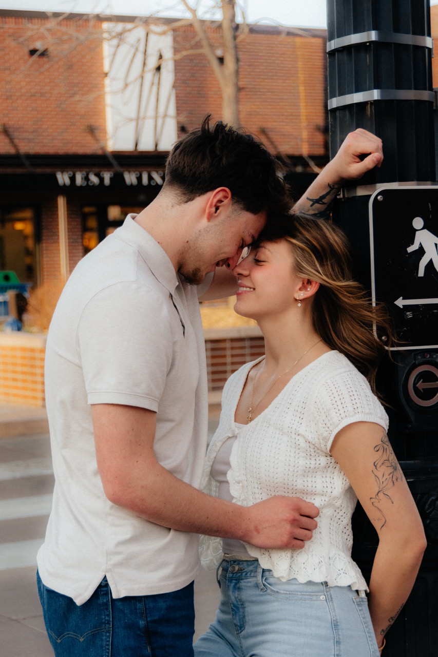 Ellie and Lane pressed forehead-to-forehead beside a black lamppost downtown