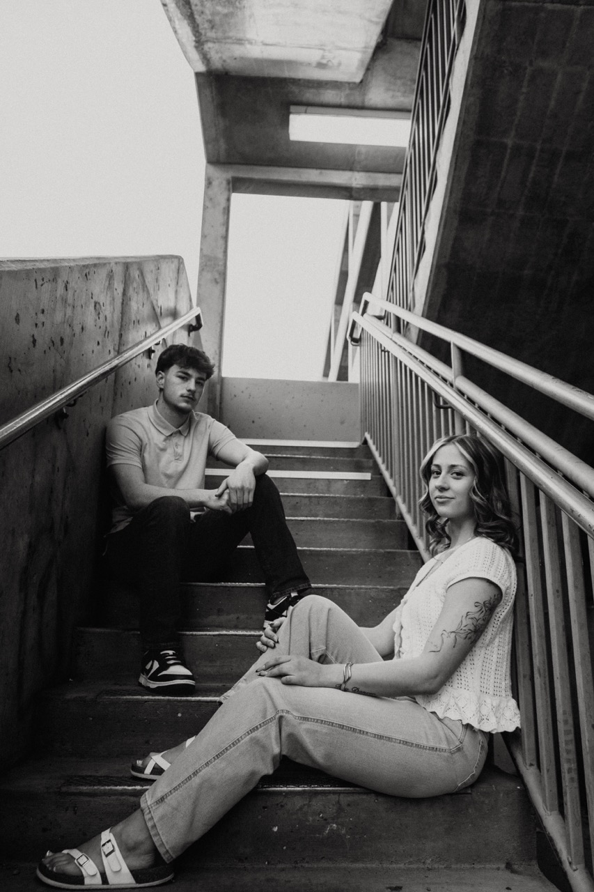 Black and white portrait of Ellie and Lane sitting apart on a concrete stairwell
