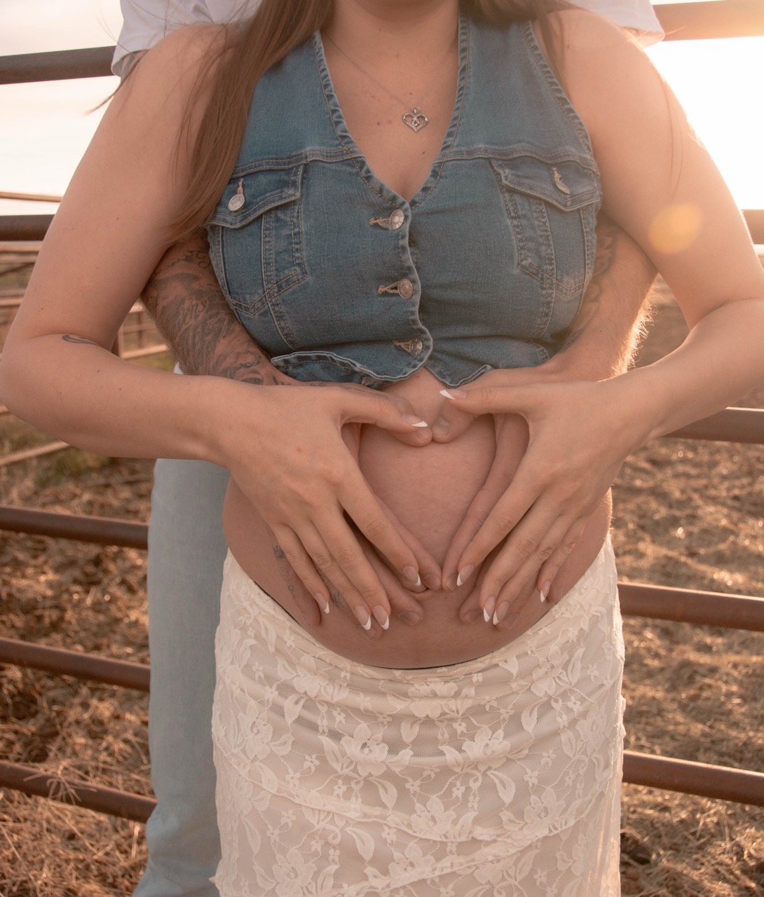 Close-up of Ashley and Kevin's hands forming a heart on her bare pregnant belly