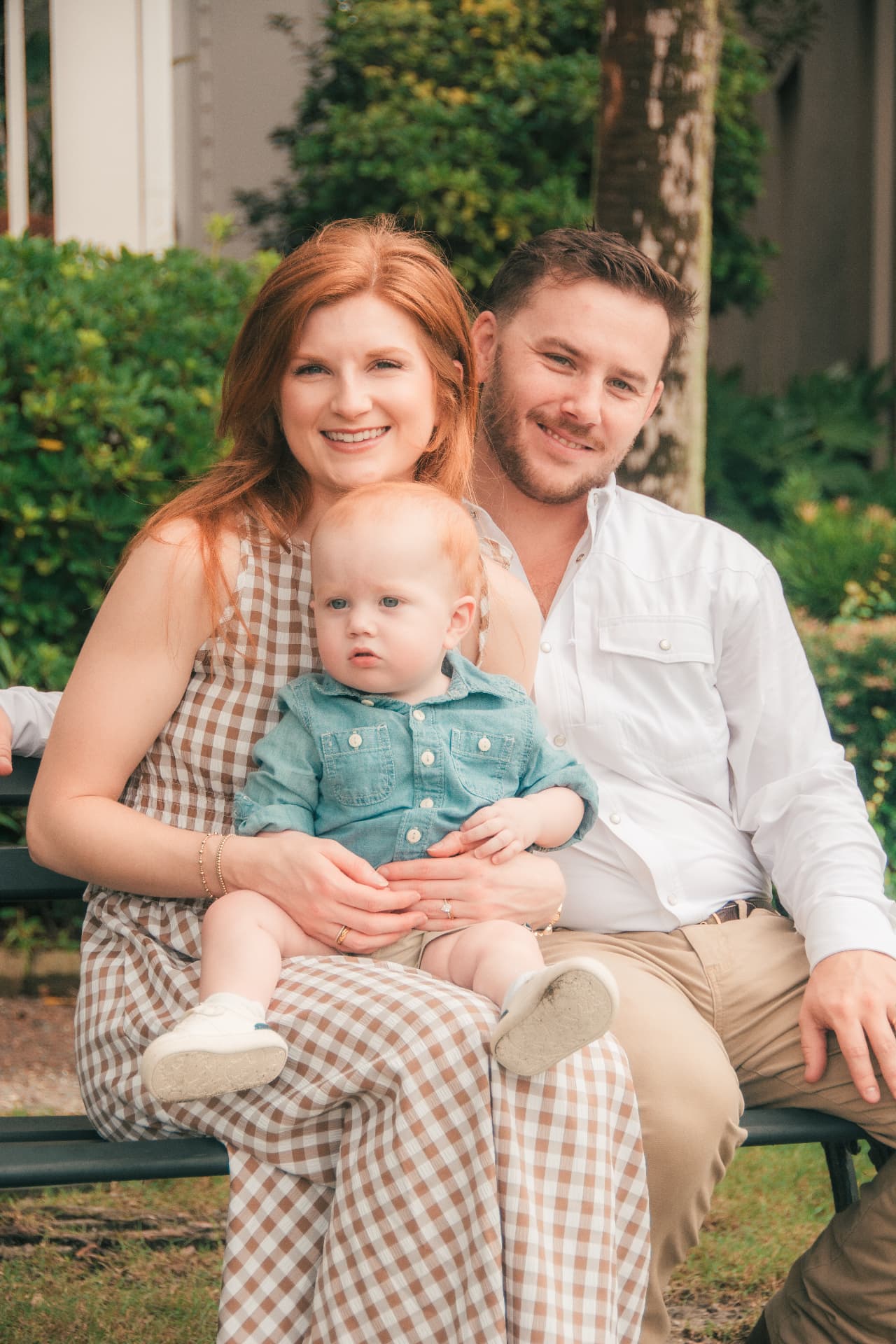 Mom and dad sitting on a garden bench with their baby boy between them