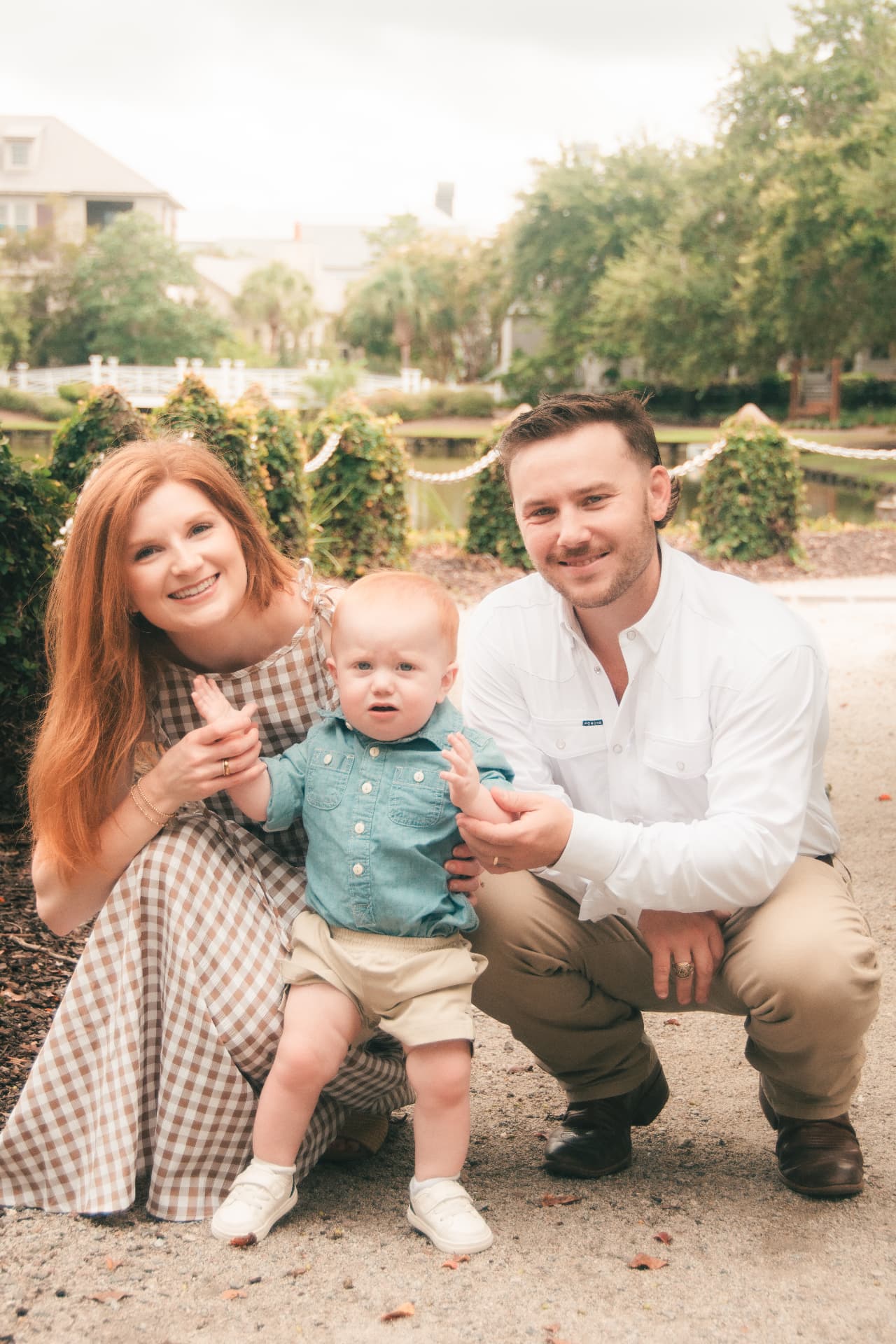 Mom, dad, and baby crouching together by the water, the lake and trees behind them