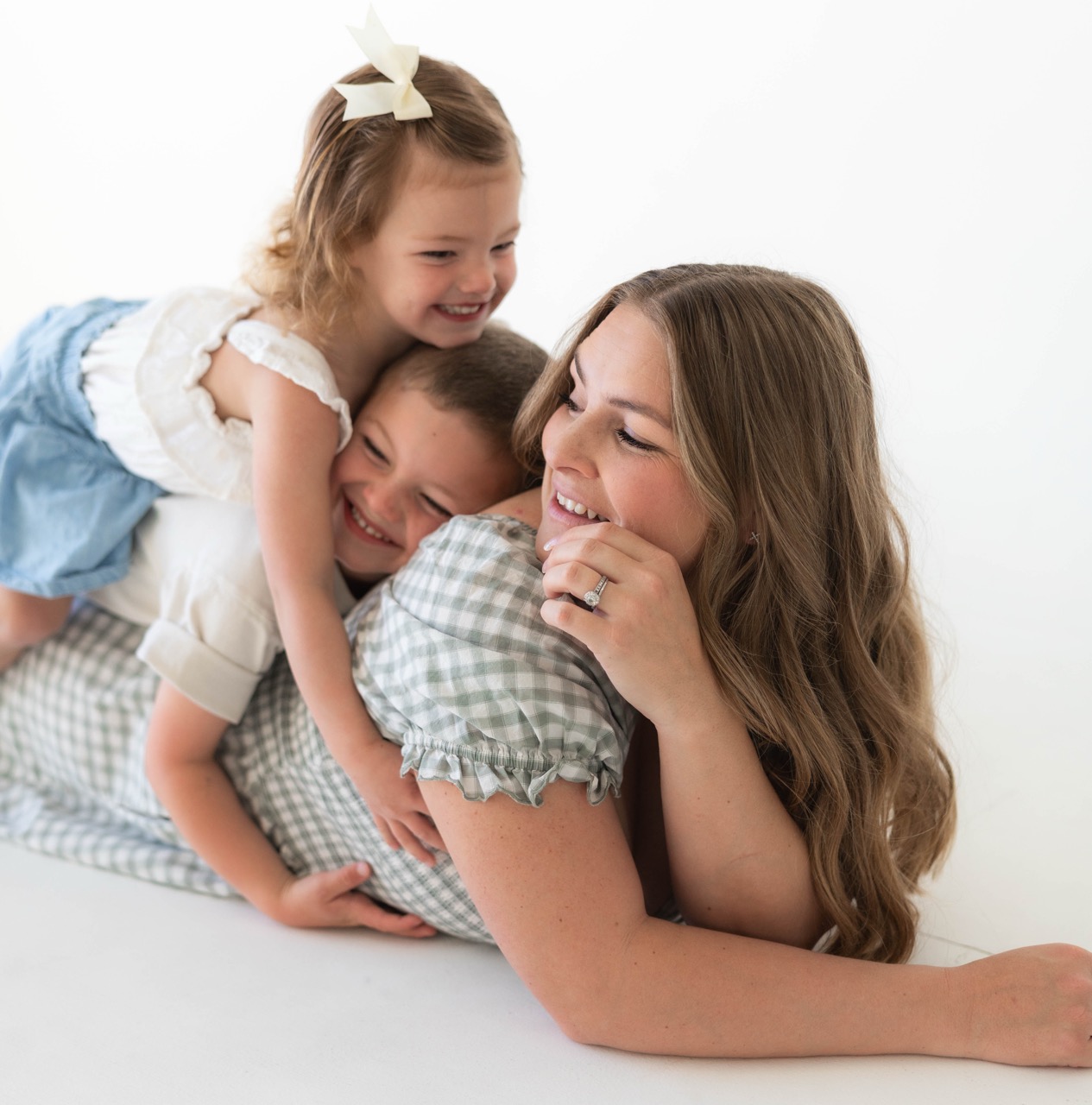 Two older siblings draped over mom as she lies on the studio floor laughing