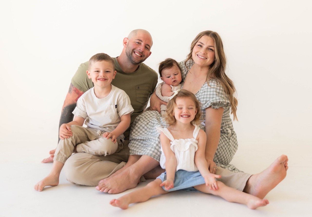 Whole family of five sitting on the studio floor, all smiling at the camera
