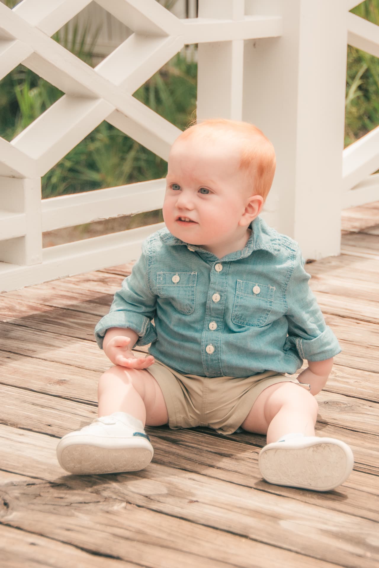 Baby boy sitting on the wooden boardwalk, turning to smile over his shoulder