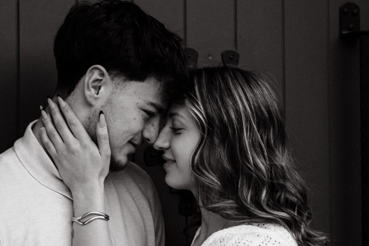 Black and white close-up of Ellie cradling Lane's face, foreheads touching