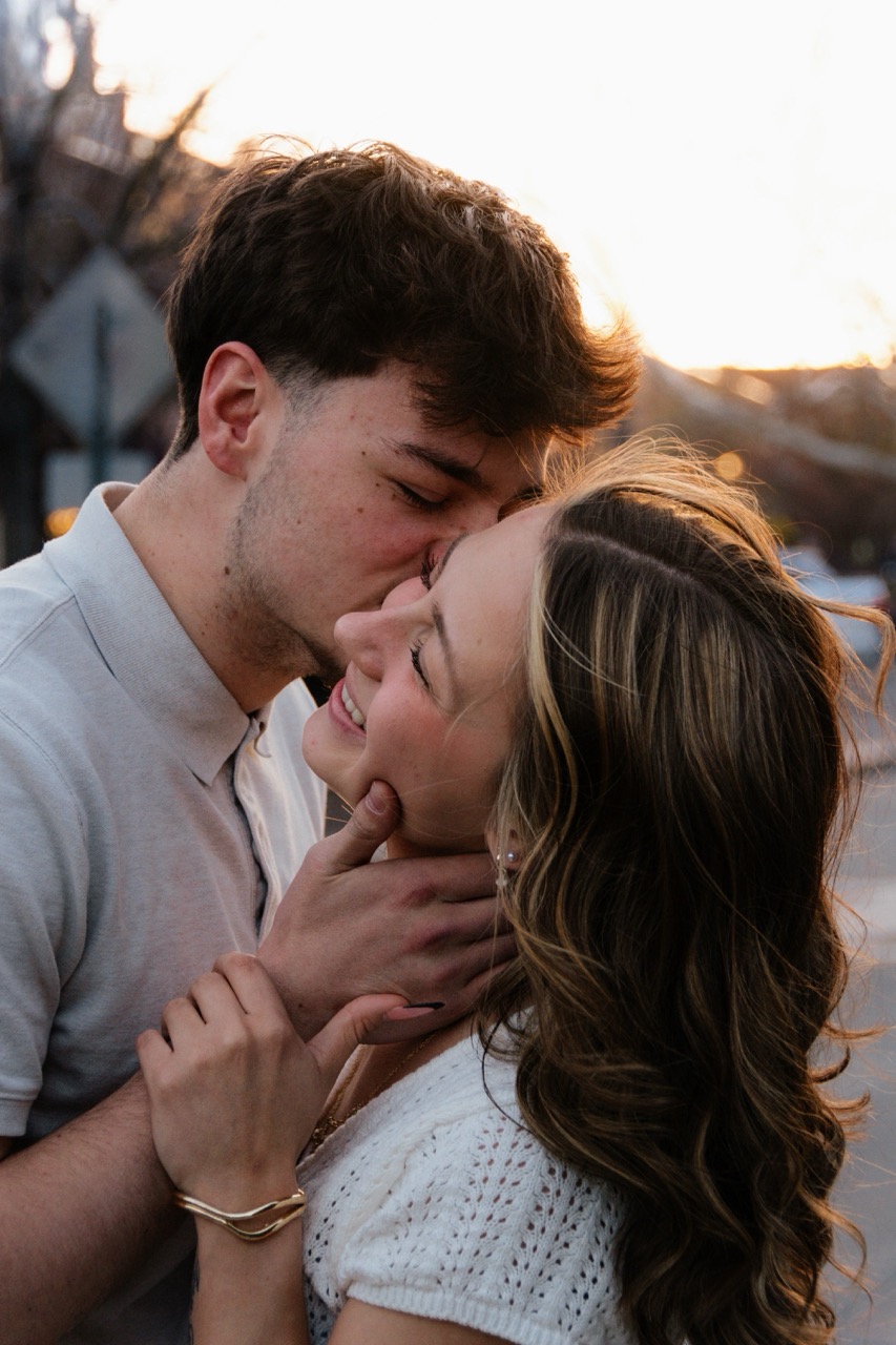 Lane kissing Ellie's forehead on a downtown street at golden hour