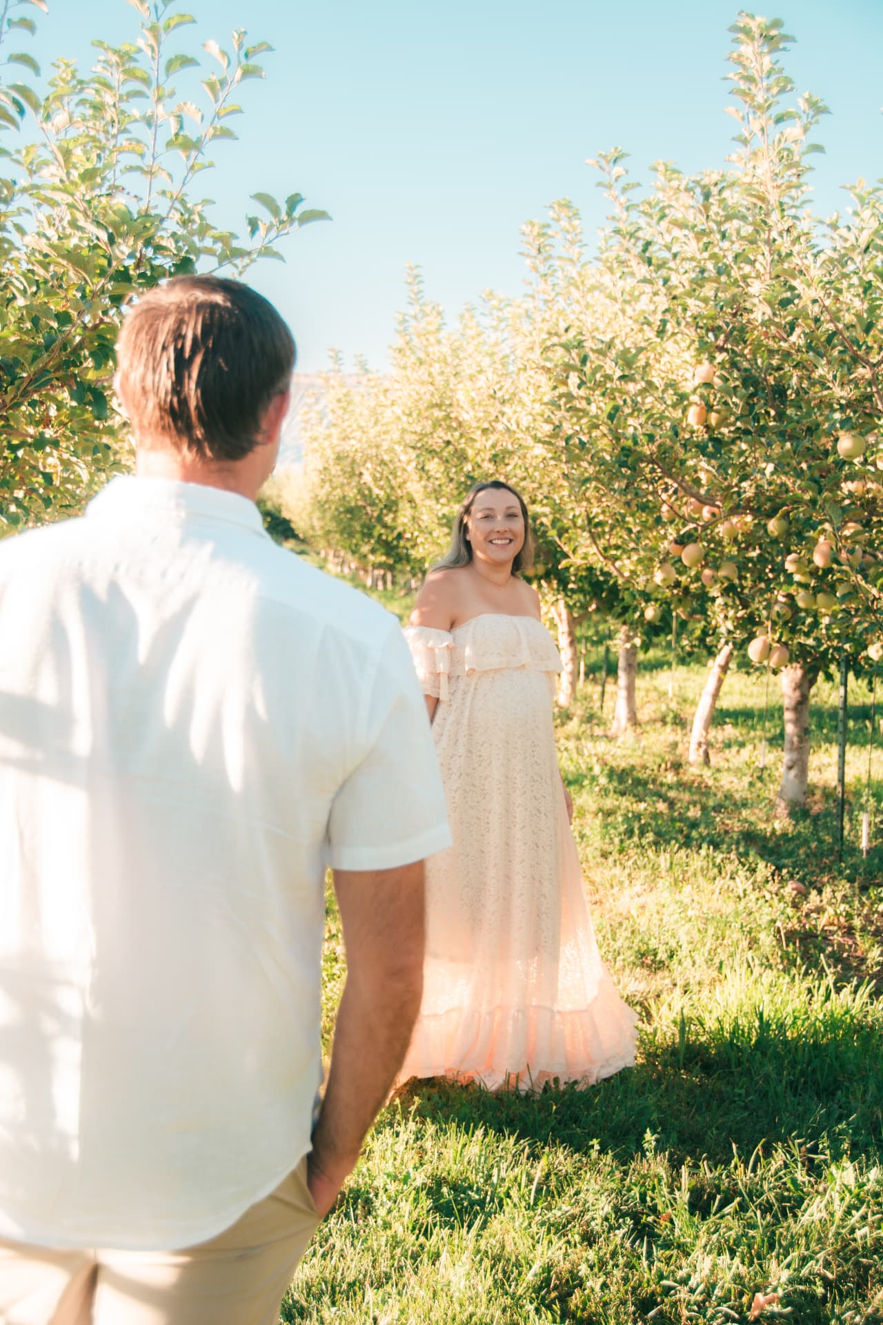 Dad-to-be watching his wife smile back at him from down the orchard row