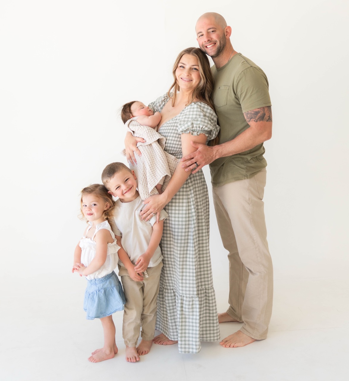 Whole family of five standing together — mom holding the baby, dad behind her, two older kids in front