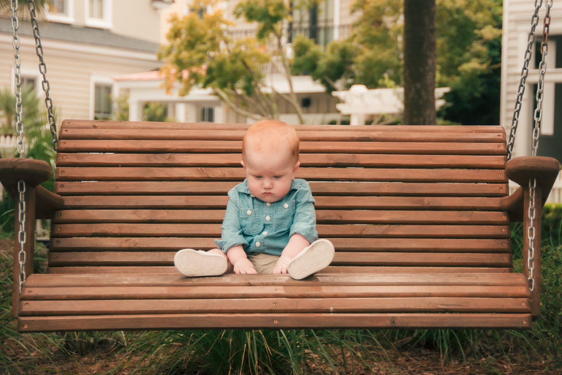 Baby boy sitting alone on a wooden porch swing in the soft evening light