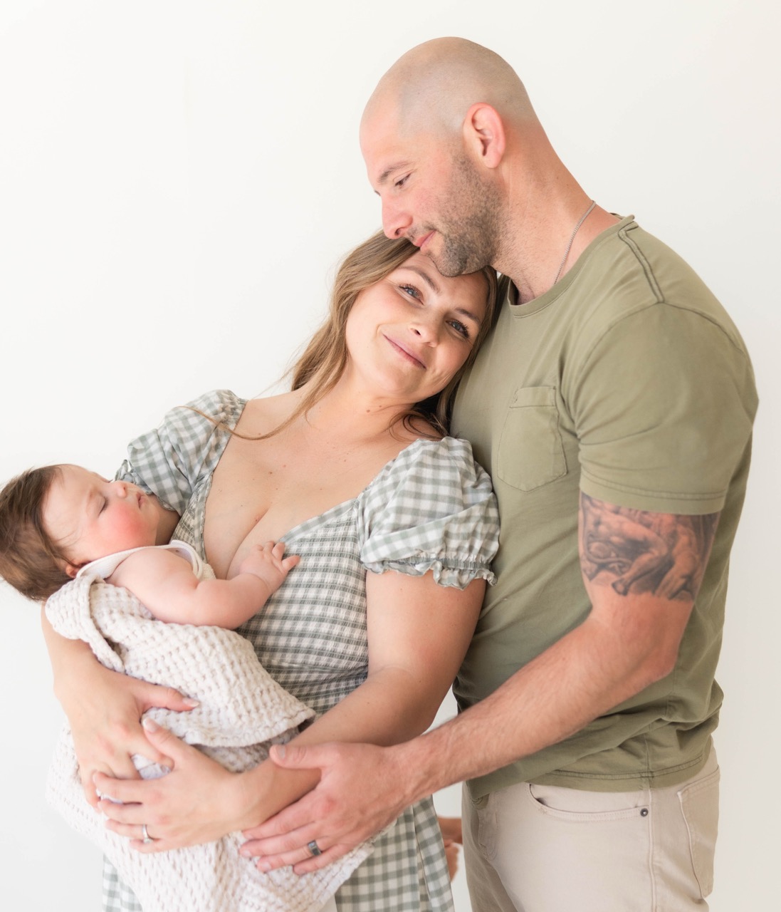 Dad kissing mom's forehead while she holds their sleeping baby against her chest