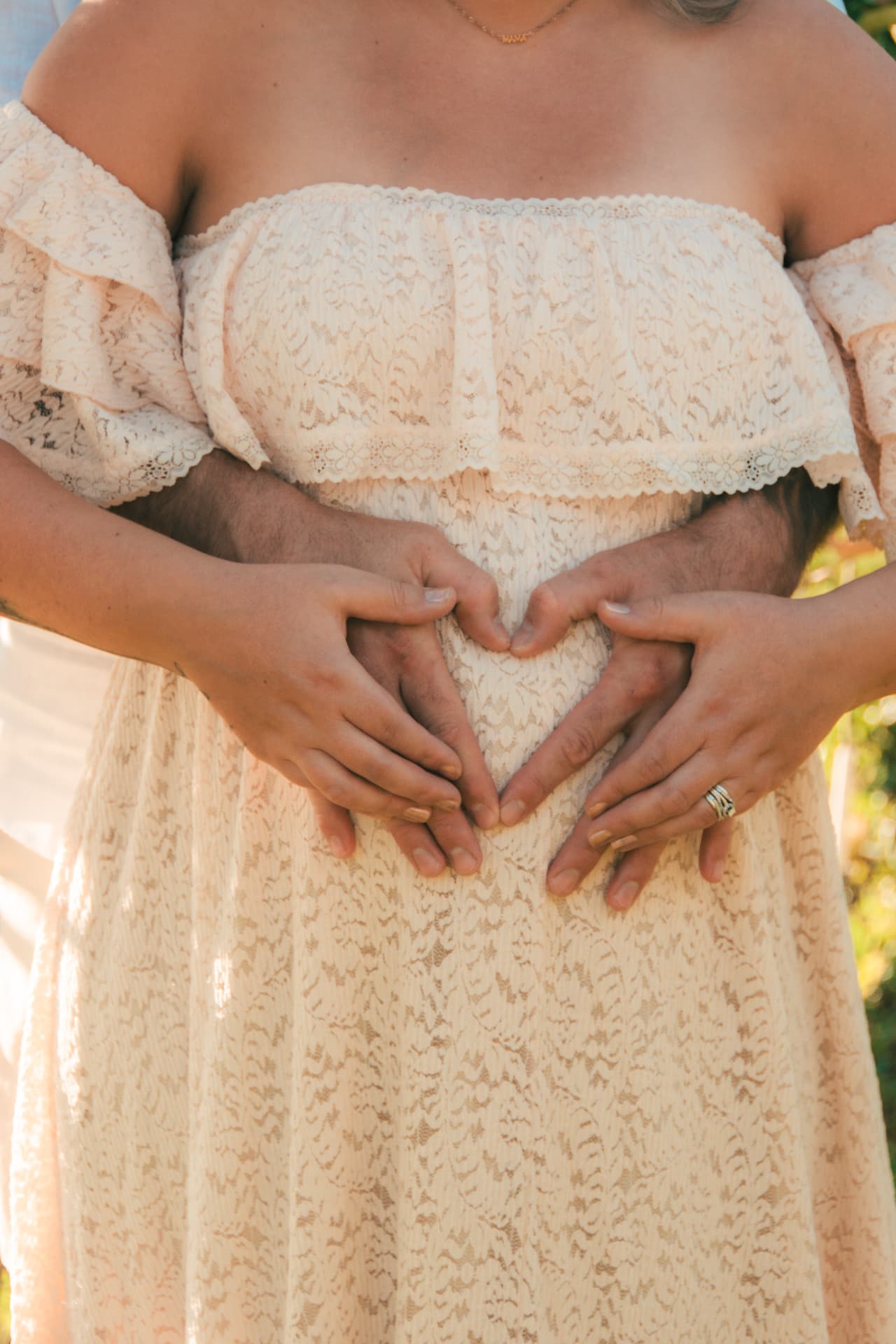 Parents-to-be forming a heart with their hands over her lace-covered belly