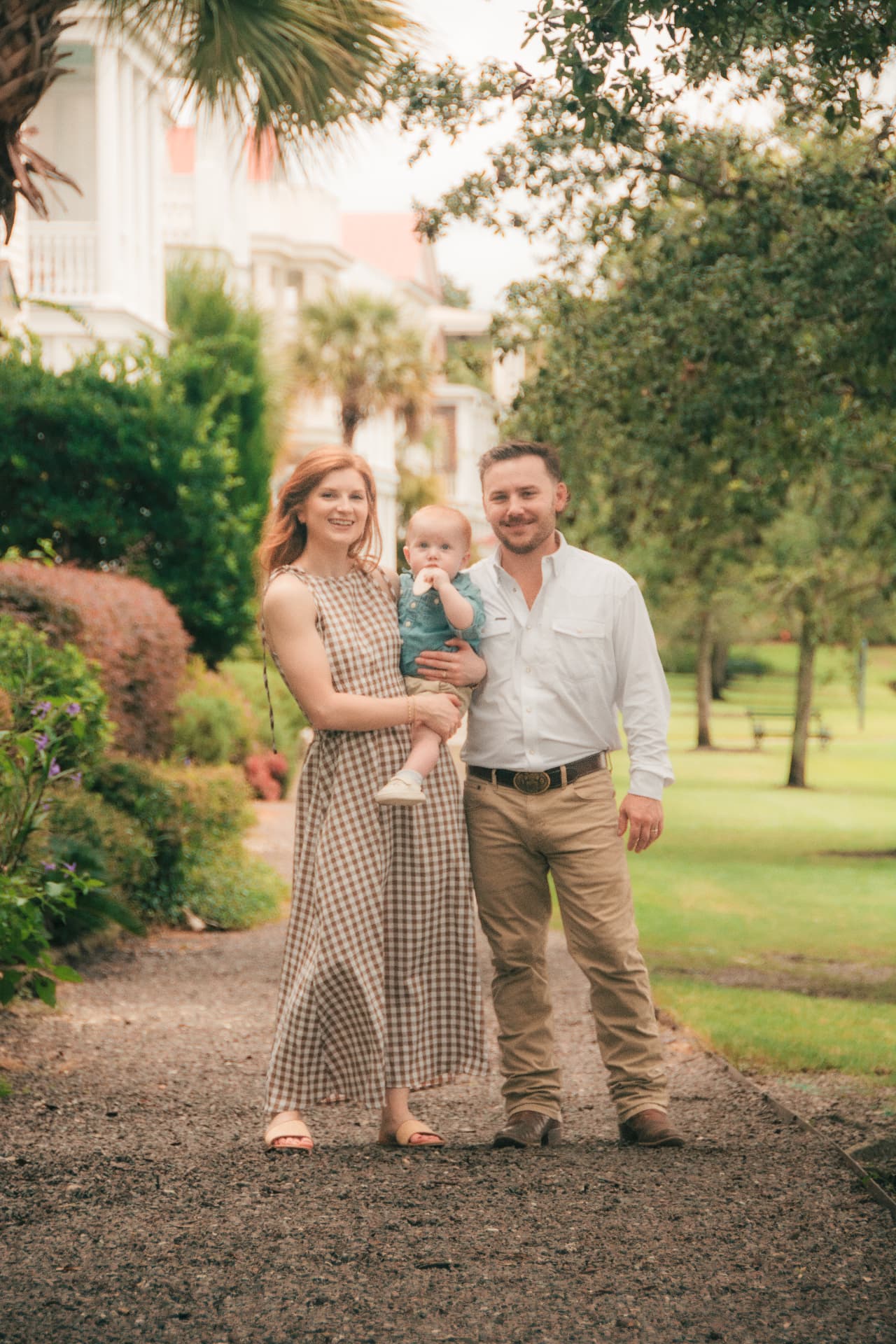 Family portrait on a gravel garden path, mom holding the baby with dad beside them