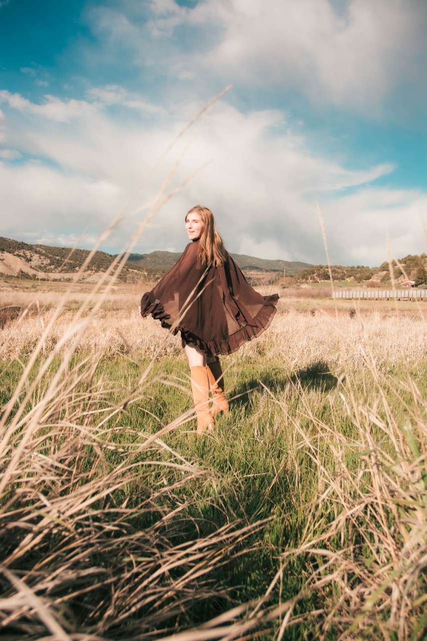 Woman in a brown chiffon kimono and tan suede boots looking back over her shoulder in a windswept field