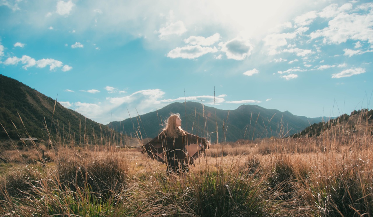 Wide shot of a woman standing in a windy meadow with mountains rising on either side
