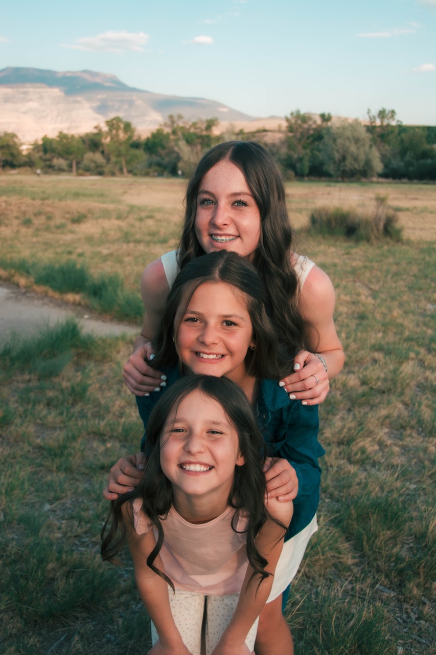 Three sisters stacked close, smiling in a sunlit meadow