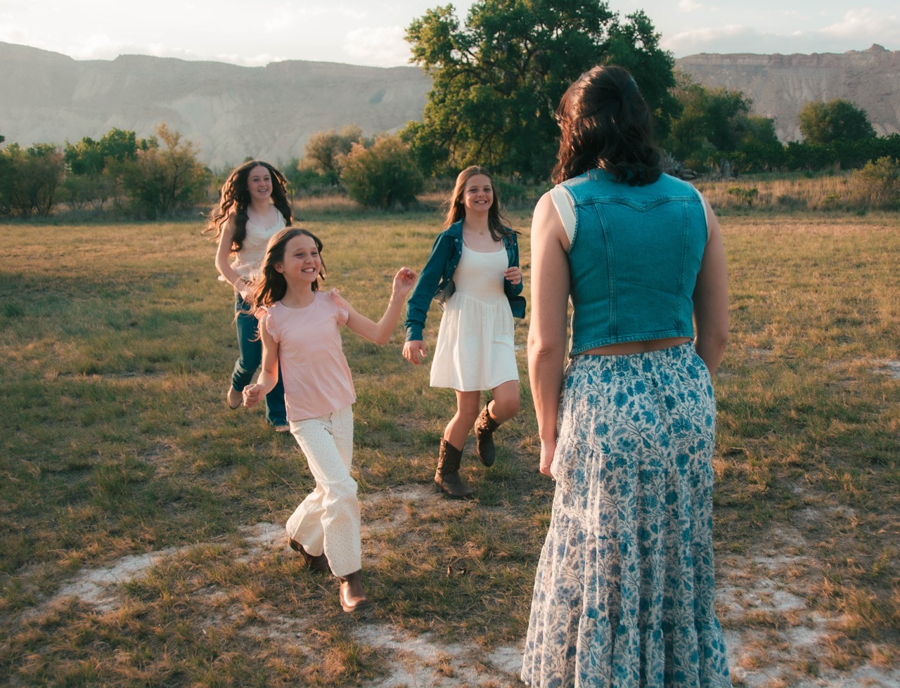 Three daughters running toward their mother in an open field at sunset