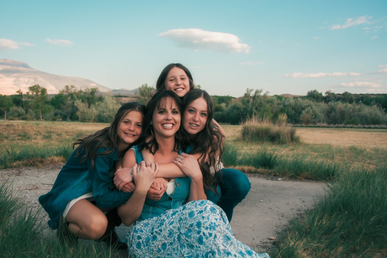 Mother sitting low while her three daughters wrap their arms around her, laughing