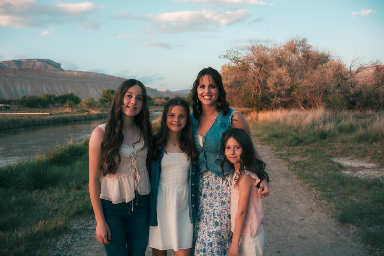 Family of four standing beside a quiet river at golden hour with mesas behind