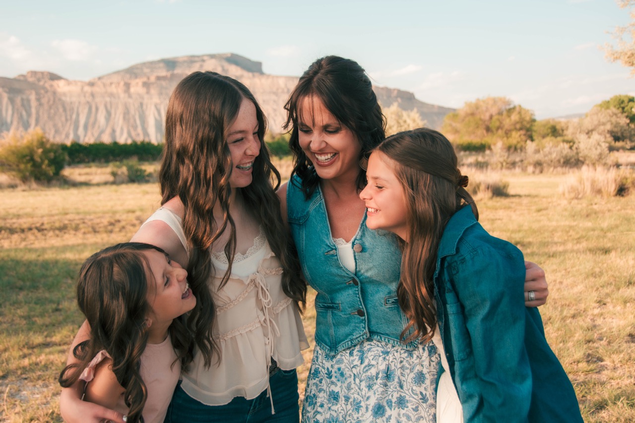 Mother laughing with her three daughters in a Colorado mesa field at golden hour